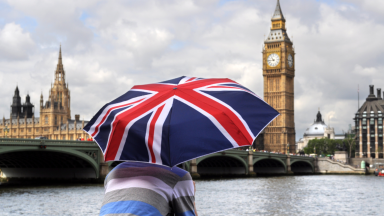 A young man watching the Big Ben in London with a UK flag umbrella.