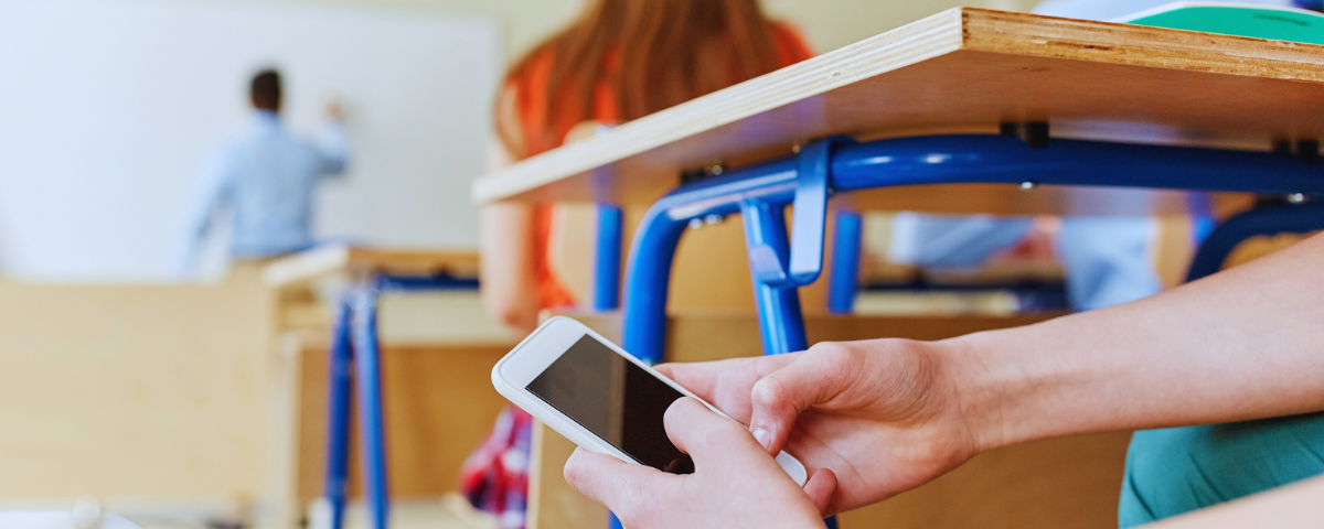 A student using cellphone in classroom while the teachers teaches.