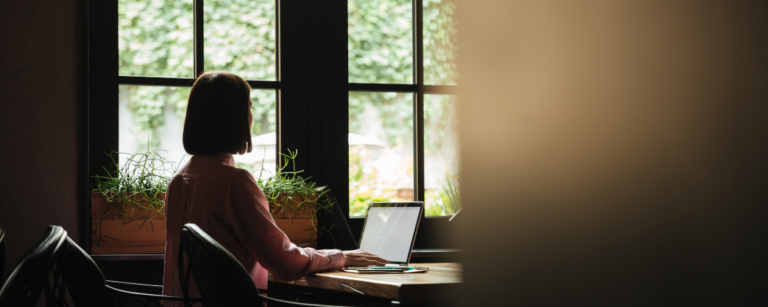 A woman working on a laptop at a desk by a window, symbolising white-collar women professionals navigating AI-driven workplace changes.