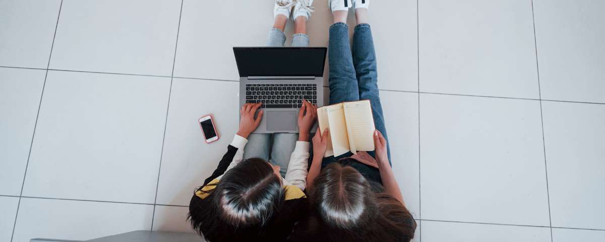 Two students sitting on the floor working on a laptop and notebook, representing growing student use of generative AI tools