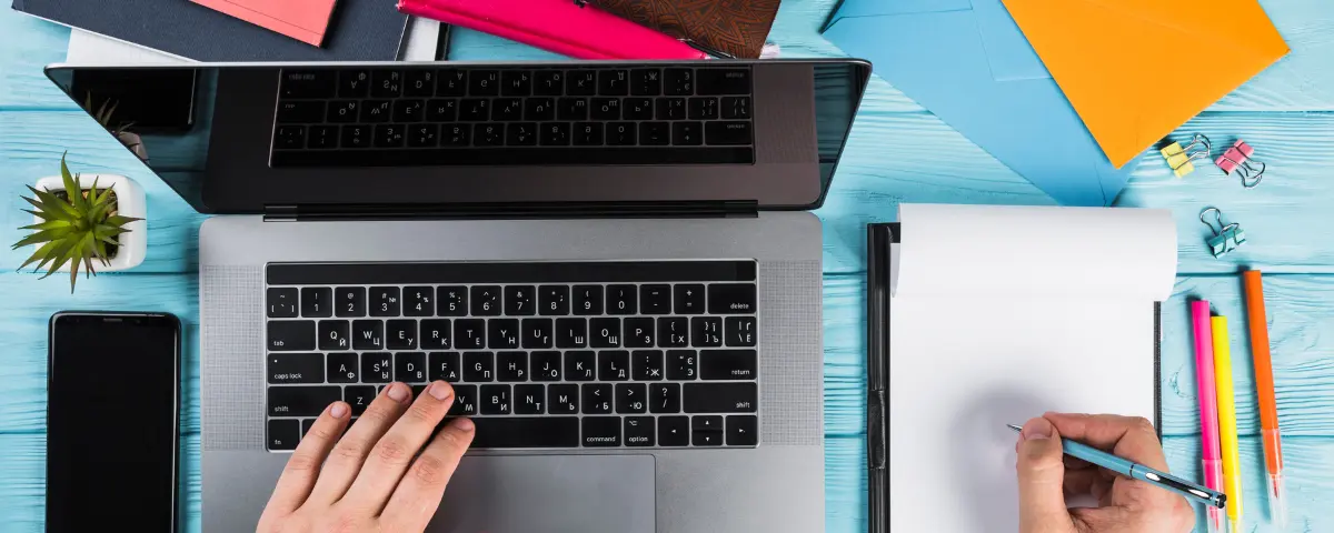 A marked university essay with pen corrections beside a laptop, illustrating AI grading of university essays
