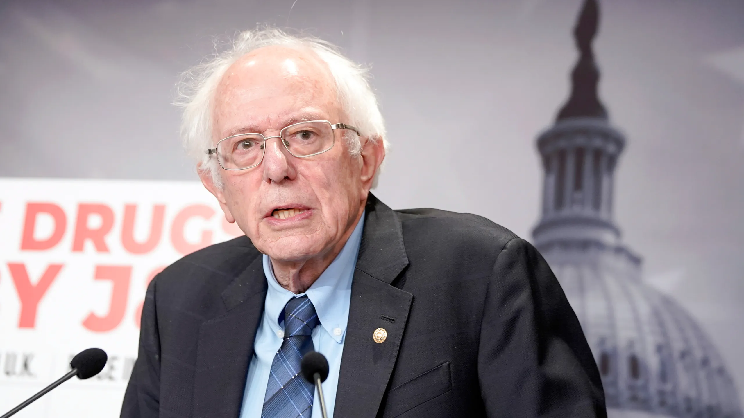 US Senator Bernie Sanders speaks at a press conference with the US Capitol visible in the background.