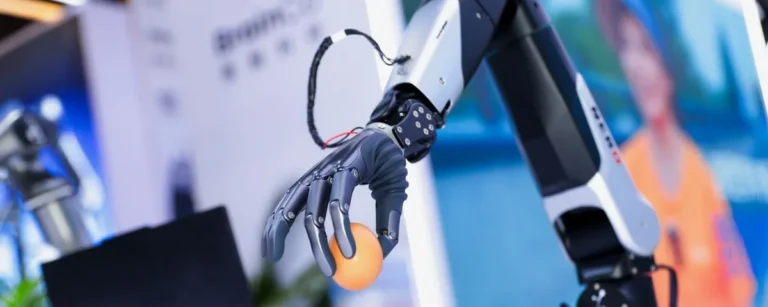 Robotic arm with a dexterous five-finger hand holding an orange ball at the BrainCo booth during WAIC 2026 in Shanghai