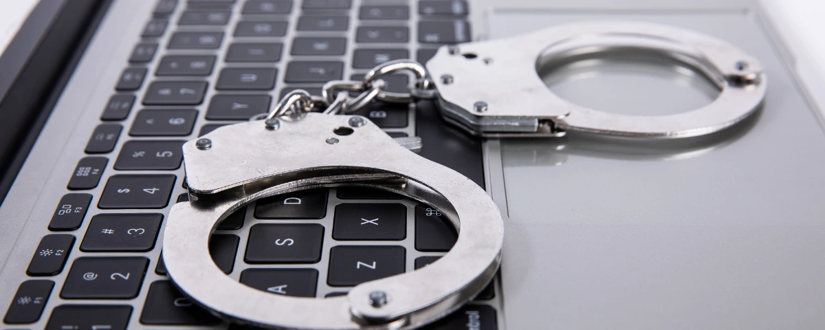 Close-up of a pair of metal handcuffs placed on the keyboard of a laptop, symbolizing cybercrime, digital fraud investigations, or online law enforcement.