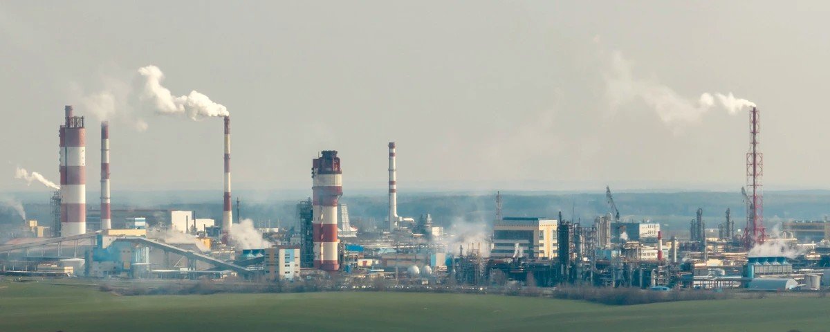 Industrial oil and gas facility with multiple smokestacks and processing units emitting plumes, illustrating methane emissions and industrial greenhouse gas monitoring.