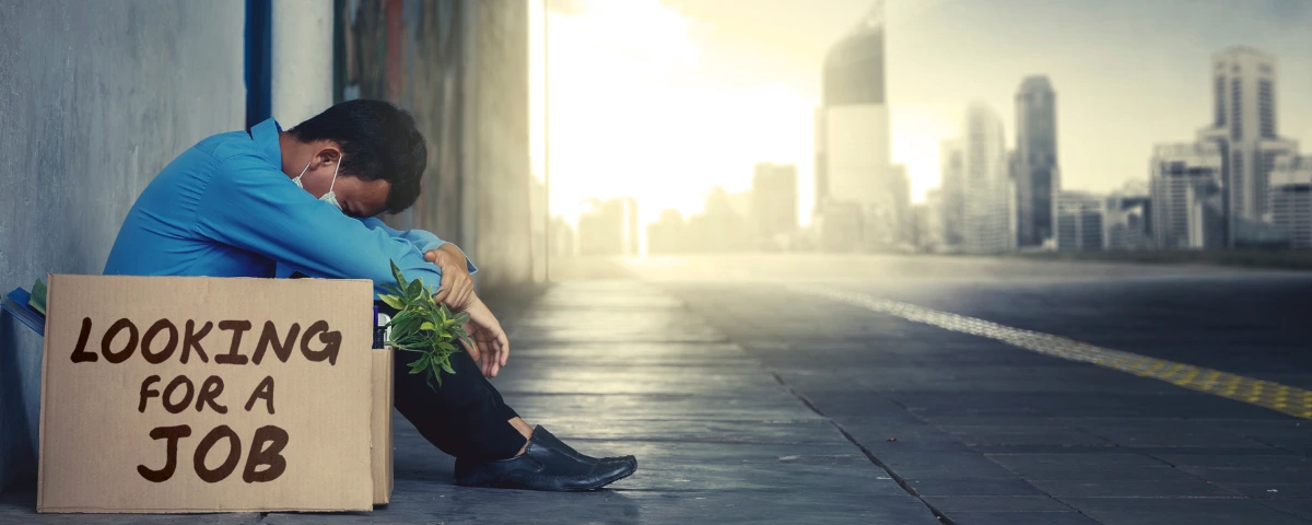 Young person sitting alone under an urban overpass beside a sign reading “Looking for a Job,” symbolizing rising youth unemployment and challenges entering the labour market.