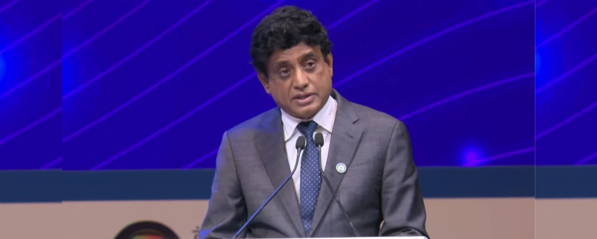 Prabhu Raja of Applied Materials speaking at a podium during SEMICON India 2026 in New Delhi, wearing a grey suit and blue tie against a blue stage backdrop.