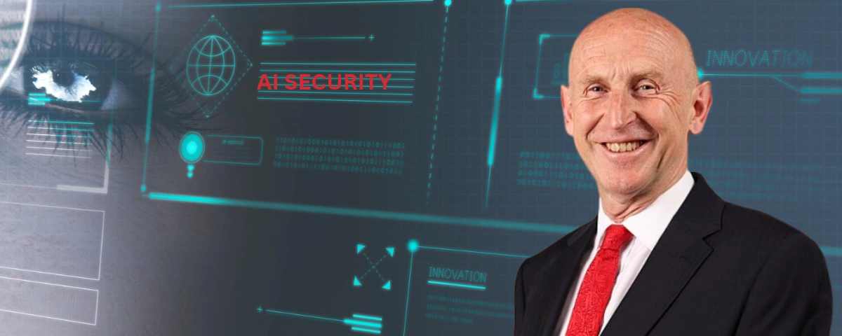 UK Chancellor John Healey stands in front of a digital background displaying AI security and innovation graphics.