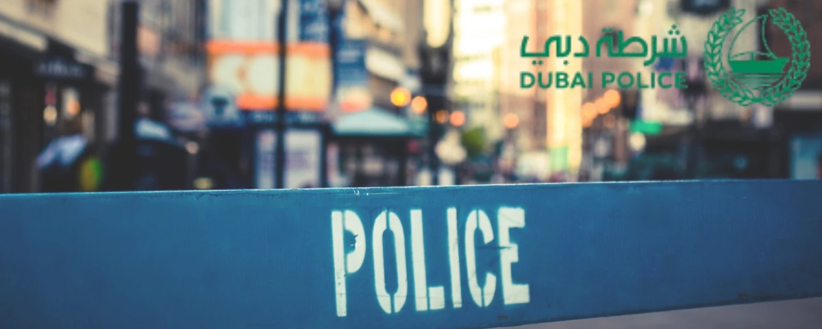 Dubai Police logo above a blue police barricade with “POLICE” lettering on a city street.